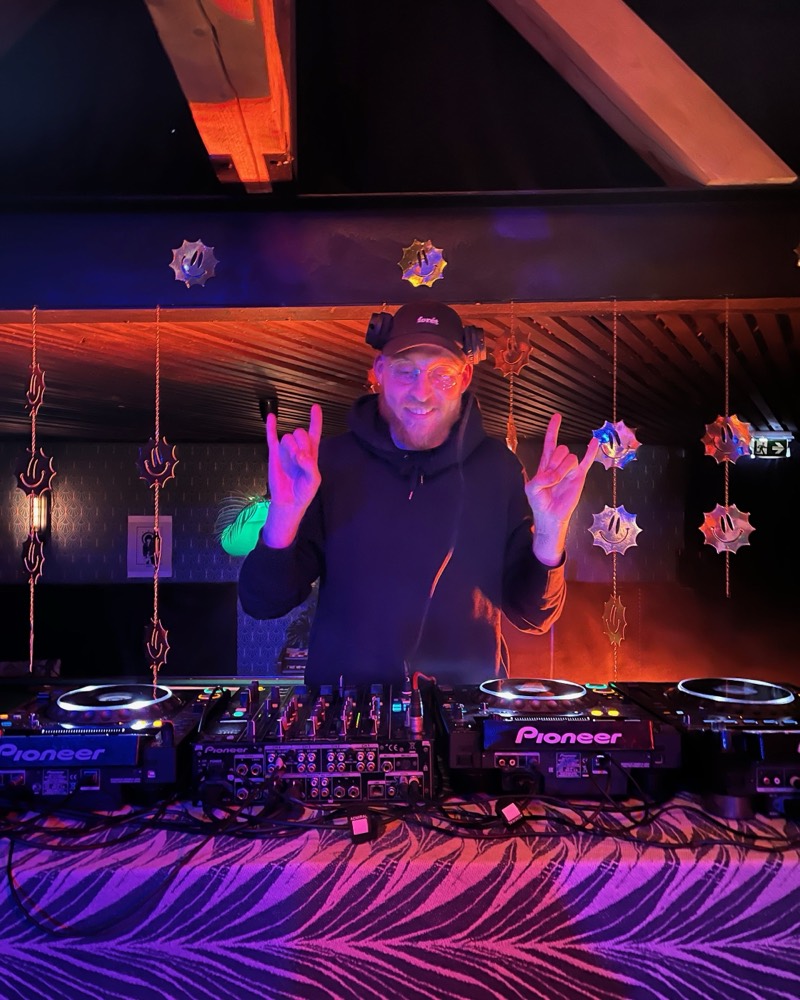 Mikk DJing behind the decks under colorful lights