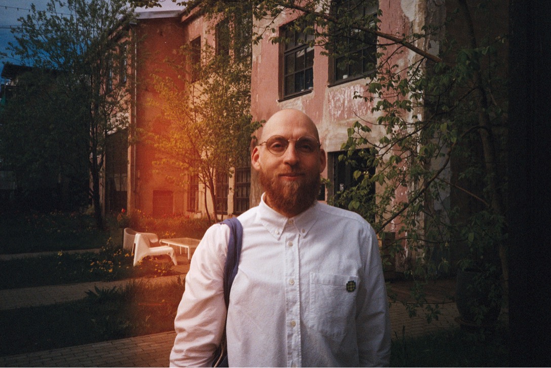 Portrait of Mikk in a white shirt, standing in a leafy courtyard
