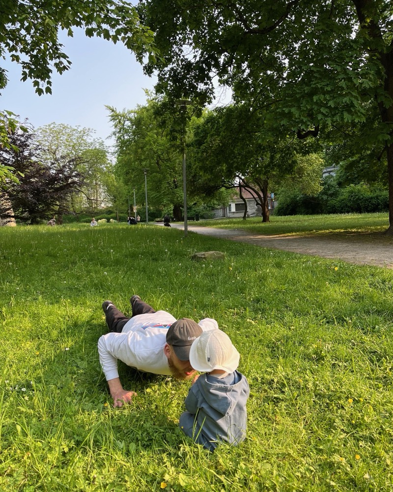 Mikk lying in the grass of a summer park with a small child