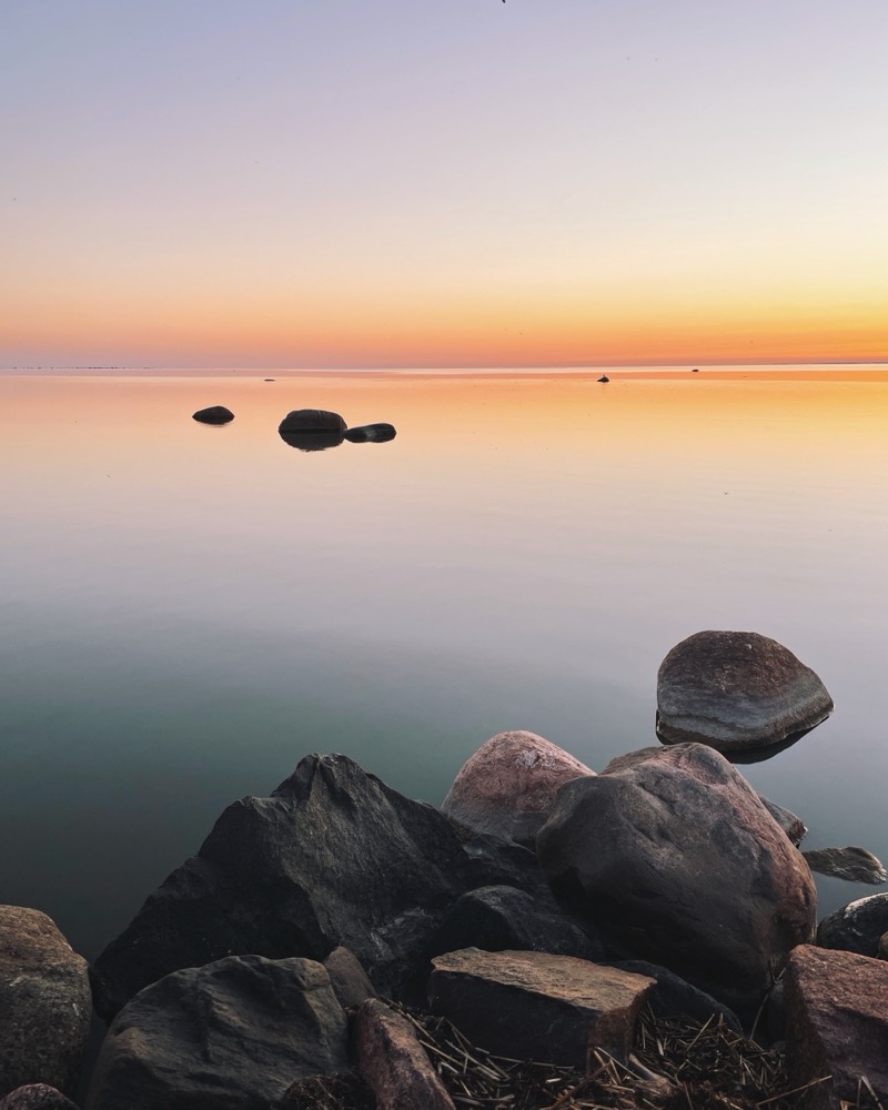 A calm sea at sunset, with rocks in the foreground